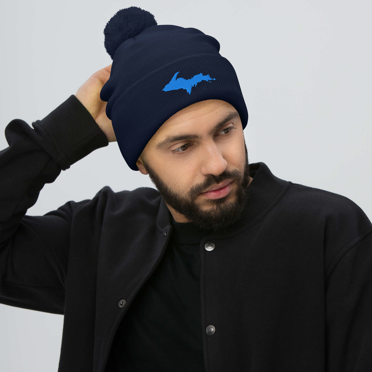 Navy Blue pom-pom beanie with Michigan's Upper Peninsula  embroidered in aqua blue on the front worn by a man.